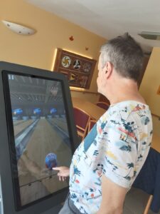 Résident jouant à un jeu interactif de bowling sur une tablette tactile XXL dans un EHPAD.